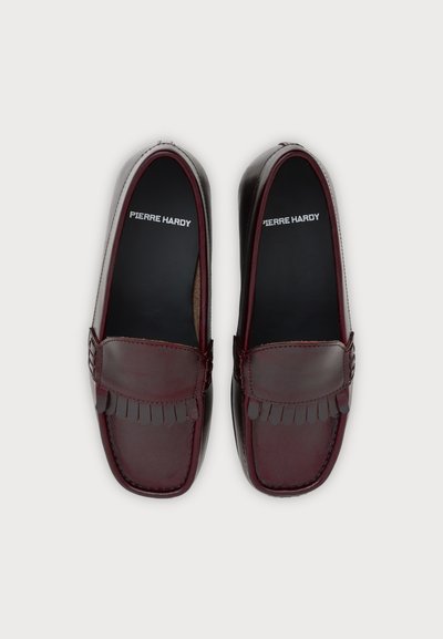 Paire de mocassins en cuir rouge foncé avec des détails à pampilles et des semelles intérieures noires griffées "Pierre Hardy" sur un fond clair uni.