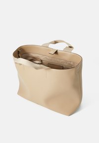Beige skinnveske med vid åpning, to håndtak og innvendige lommer. Glatt tekstur med minimalistisk design.