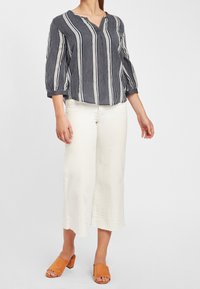 Marynarska bluzka w białe paski z dekoltem w serek i rękawami o długości trzech kwadransów, zestawiona z białymi spodniami o szerokich nogawkach i brązowymi klapkami na obcasie.