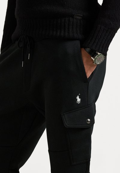 Svarta joggers med en cargo ficka, tillverkade av mjukt tyg. Har en vit broderad logotyp och justerbara dragsko i midjan.