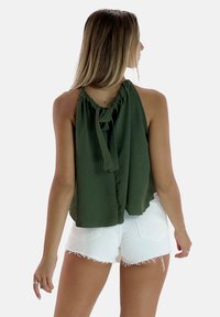 Top halter verde oliva con un nodo sul retro, caratterizzato da una vestibilità ampia e tessuto texturizzato. Abbinato a pantaloni corti bianchi sdruciti.