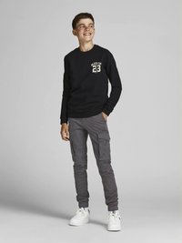 Černé tričko s dlouhým rukávem s grafikou a číslem 23, doplněné šedými cargo kalhotami a bílými teniskami. Jednoduchý design, volný střih.