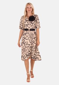Beige Midi-Kleid mit floralen Muster und schwarzen Konturen. Verfügt über einen Gürtel und einen Stoffblumenakzent auf der Schulter. Weiches, fließendes Material.