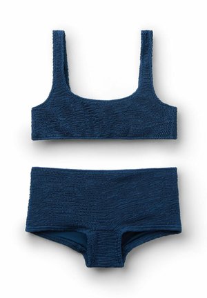 Mørkeblå tekstureret badedragt i to dele med en top med firkantet halsudskæring og højtaljede trusser, lagt fladt på en hvid baggrund.