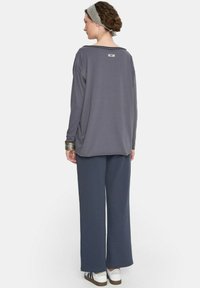 Szary longsleeve z luźnym krojem i okrągłym dekoltem, w zestawie z szerokimi szarymi spodniami. Wyraźne szerokie mankiety i metka z tyłu.