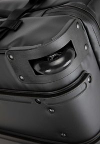 Angolo di una valigia a rotelle nera con un manico in plastica robusta e una serie di ruote lisce e lucide inserite in una base texture.