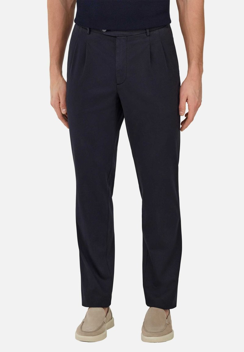 Navy blue chinos with a smooth texture, featuring front pleats, belt loops, and a tailored fit. Worn with light-colored slip-on shoes.
