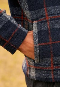 Blau-graues karierter Fleece-Pullover mit weicher Textur; mit roten Akzenten und einer Seitentasche, in lockerem Schnitt.