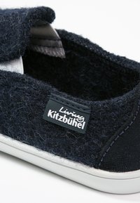 Scarpa slip-on di un blu navy scuro realizzata in lana testurizzata con suola in gomma bianca. Presenta un'etichetta con il marchio "Living Kitzbühel" e cuciture a contrasto.