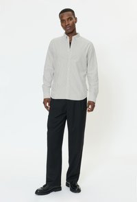 Vaaleanharmaa, raidallinen nappipaita, jossa kauluksellinen pääntie, yhdistetty mustiin, leveälahkeisiin housuihin ja mustiin nauhakenkiin.