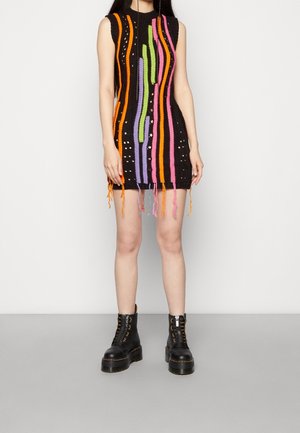 Ærmeløs sort strikket minikjole med lodrette orange, pink, grønne og lilla striber og frynser, båret med sorte plateau snørestøvler.