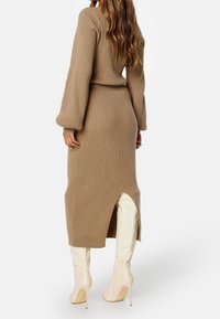 Robe pull tricotée beige à côtes avec de longues manches ballon et une fente haute dans le dos, assortie à des bottes à talons hauts crème.