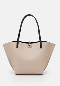 Sac cabas beige texturé avec poignées noires et un charm argenté du logo Guess au centre devant sur un fond uni.