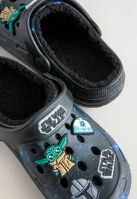 Zwarte Crocs met een pluche interieur hebben uitsparingsgaten, een ruimte-thema ontwerp en decoratieve Star Wars karakter charms.