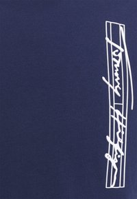 Námořnická modrá bavlněná tričko s bílým vyšitým logo designem s plynulými liniemi, umístěným ve středu na přední straně.