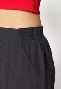 Pantaloni sportivi neri con un design plissettato, vita elastica e tasche laterali. Il materiale sembra leggero e liscio.