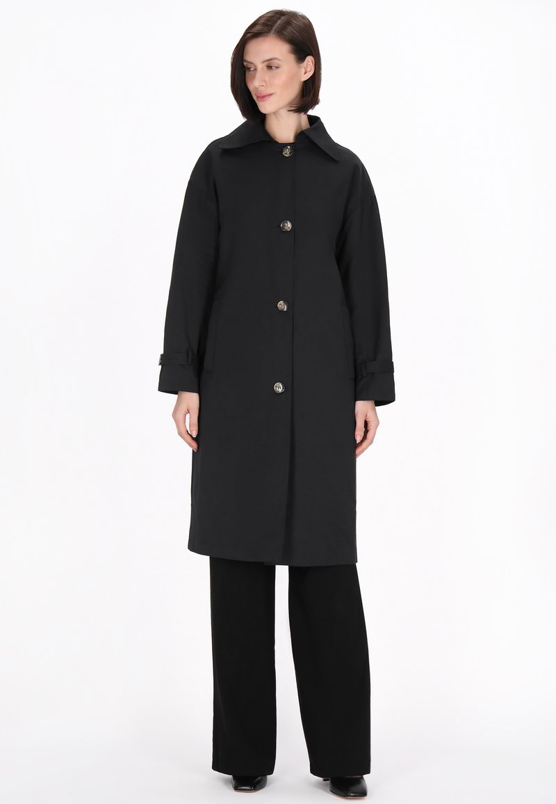 Schwarzer Trenchcoat mit großem Kragen, großen Knöpfen und langen Ärmeln. Hat einen geraden Schnitt und ist aus glattem Stoff gefertigt.
