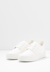 Sneaker bianche in tela con punta rotonda, design minimalista, suola in gomma piatta e chiusura con lacci caratterizzata da cinque occhielli.