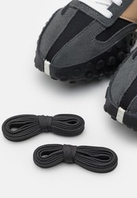 Šedé sportovní boty vyrobené z materiálů s textilem a semišem, s texturovanou černou podrážkou a bílými tkaničkami, doplněné o dvě černé tkaničky.