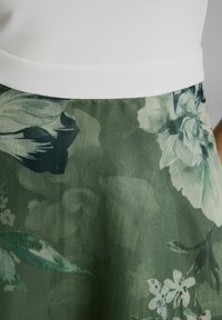 Gonna con stampa floreale in tonalità di verde, caratterizzata da una texture plissettata e una ampia vita bianca per una vestibilità definita. Accenti includono foglie scure.