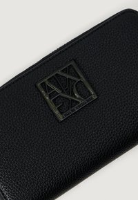 Czarny portfel ze strukturalnej skóry z zamkiem, z kwadratową czarną metalową plakietką logo Armani Exchange z przodu.