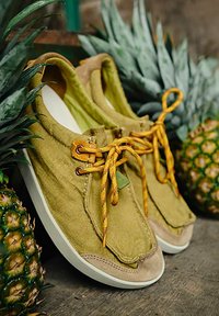 Sneakers in tela verde con lacci gialli, accenti in suede e suole in gomma bianca. Presentano una punta arrotondata e dettagli di cucitura.