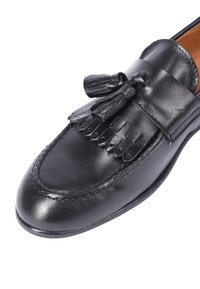 Mocassino in pelle nera con punta rotonda, caratterizzato da dettagli frangiati e nappine sulla tomaia, cuciture decorative e una finitura liscia e lucida.