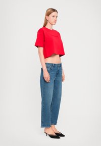Tricou scurt roșu cu mâneci scurte, blugi din denim albastru și pantofi cu toc kitten-heel negri. Ținuta are un design casual, modern.