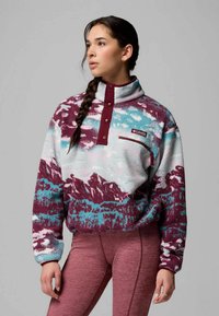 Pulóver de forro polar con cuello alto, patrón de montañas multicolor en tonos de púrpura, azul y blanco, que incluye un bolsillo en el pecho y botones.