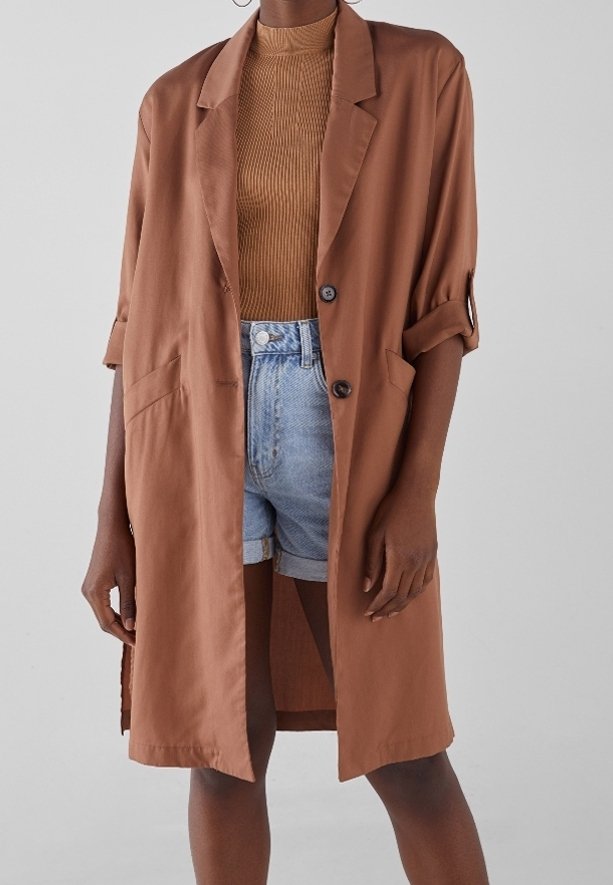 Brązowa oversize marynarka z gładkiego materiału, z wykrojonym kołnierzem, zapięciem na pojedynczy guzik i dwoma przednimi kieszeniami. Można połączyć z dżinsowymi szortami.