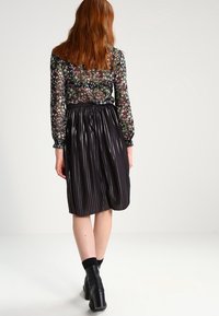 Blouse à manches longues florale en tissu noir transparent ; comprend une jupe plissée en satin noir, longueur genou, avec une texture lisse et une taille élastique.