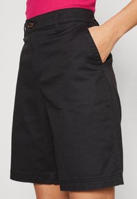 Zwarte katoenen korte broek met een knoopsluiting aan de voorkant, zijzakken en nette stiksels. Halverwege de dijen, met een recht gesneden ontwerp.