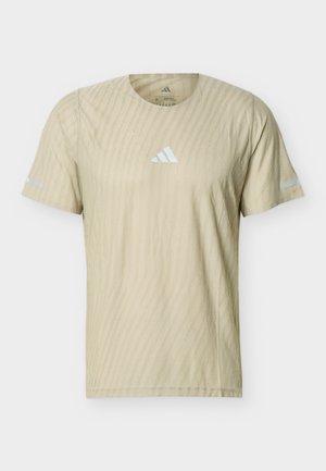 Beżowa sportowa koszulka z krótkim rękawem o delikatnej diagonalnej fakturze, okrągłym dekolcie i małym białym logo Adidas na środku klatki piersiowej.