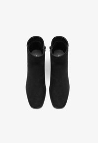 Mustadest sametist ankle botased saledaga, ruutpeaga ja külgmiste tõmblukkudega; minimalistlik disain saleda silueti poolest.