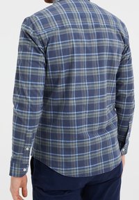 Pánská košile s dlouhým rukávem v kostkovaném vzoru v námořnické modré a světle zelené barvě. Bavlněná látka s knoflíkovými manžetami a zaobleným lemem, zdobená kostkovaným vzorem.