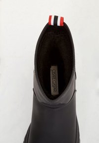 Botín negro con un exterior liso, forro texturizado y una tira de sujeción roja, blanca y negra en el talón.