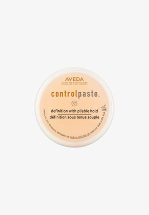 Aveda Control Paste w okrągłym, przejrzystym opakowaniu. Etykieta produktu w jasnym odcieniu brzoskwiniowym z czarnym tekstem opisującym elastyczne trzymanie i definicję.