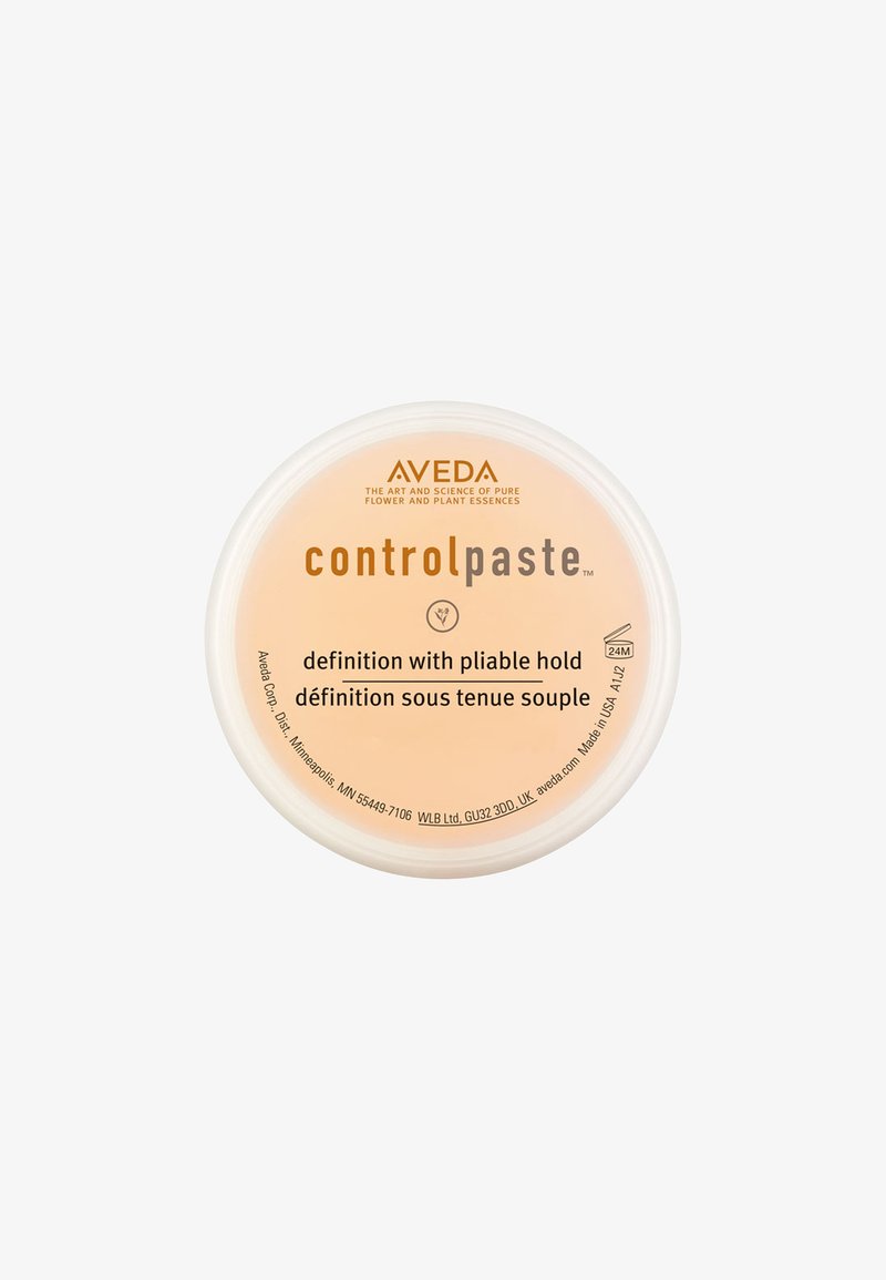 Aveda Control Paste in einem runden, transparenten Behälter. Das hellpeachfarbene Produktetikett zeigt schwarzen Text, der von flexibler Haltbarkeit und Definition spricht.