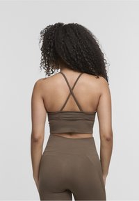 Top sportivo marrone con spalline incrociate e design aderente, realizzato in un tessuto liscio. Accentuato da una cucitura orizzontale vicino alla vita.