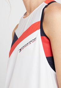 Top atlético sin mangas en blanco, con acentos en rojo y azul marino. Panel superior de malla, con un logotipo y un diseño de bloques de color geométrico.
