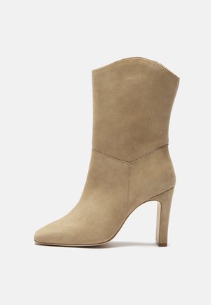Botte mi-mollet en daim beige avec bout pointu et talon bloc haut, présentant un bord supérieur légèrement incurvé et une texture lisse.
