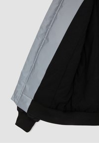 Black and gray puffer jacket interior featuring smooth lining, elastic cuffs, and ribbed hem. Includes contrasting fabric sections.