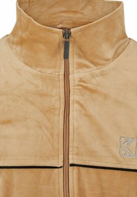 Bežna jakna na zadrgo iz mehkega, gladkega materiala. Ima visoki ovratnik, kontrastne črne šive in majhen logotip na predelu prsih.