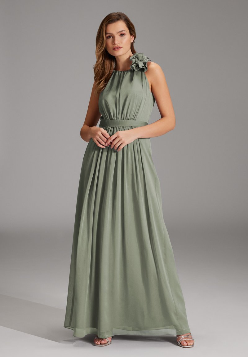 Lange mouwloze jurk in saliegroen, met een verzameld lijfje, elastische taille en een ruchesbloemdetail op de linkerschouder.