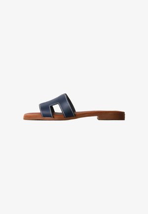Flad brun sandal med en bred mørkeblå læderrem med geometrisk udskæring og hvid syning på hvid baggrund.