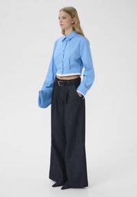 Chemise bleu clair recadrée à manches longues, associée à un pantalon large en denim foncé taille haute. Comprend une ceinture noire et une pochette bleue duveteuse.