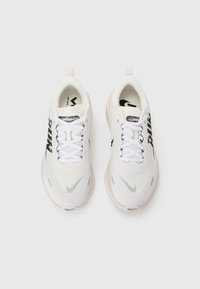 White athletic shoes with a mesh upper, black logo accents, and round toe. Features white laces and a cushioned sole for comfort.
