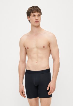 Čierne boxerky s logom na opasku, vyrobené z hladkého, elastického materiálu, priliehavý strih, dĺžka po stred stehien a minimálne švy.