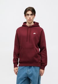 Bordový mikina s predným vreckom a kapucňou so šnúrkou, s malým bielym logom Nike na hrudi. Vyrobená z mäkkej látky.