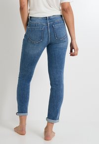 Vaqueros skinny azules de mezclilla, con cintura alta, dobladillos enrollados y dos bolsillos traseros con sutilezas en los detalles de costura.